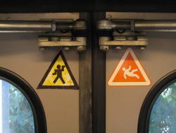 a "guerilla" sign: walk like an egyptian, and a "normal" sign: "warning: do not lean against these doors" on the inside of train doors